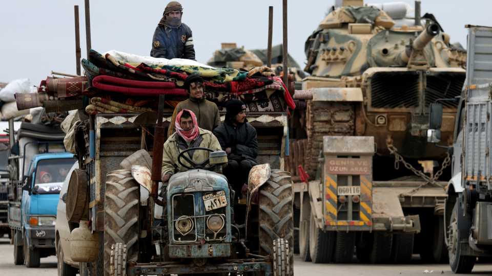 Internally displaced Syrians from western Aleppo countryside, ride on a tractor with belongings past Turkish military vehicles in Hazano near Idlib, Syria, February 11, 2020.