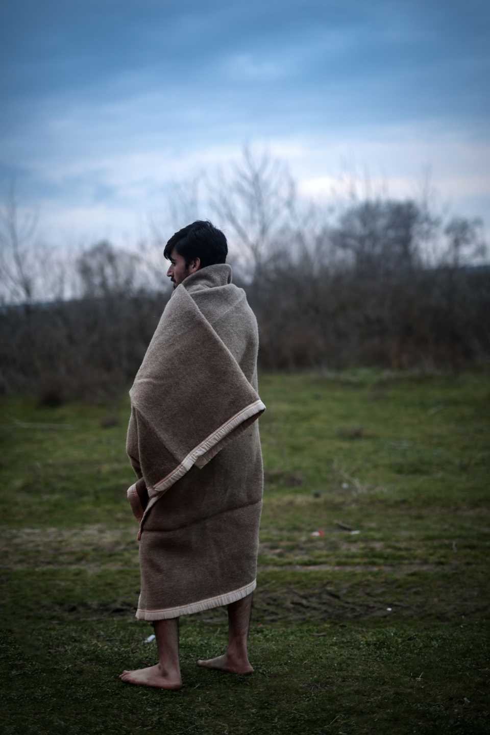 A Young man is covering himself with blanket after losing their clothes to the Greek authorities who have sent them back to Turkey without their belongings. (Belal Khaled / TRT Arabi)