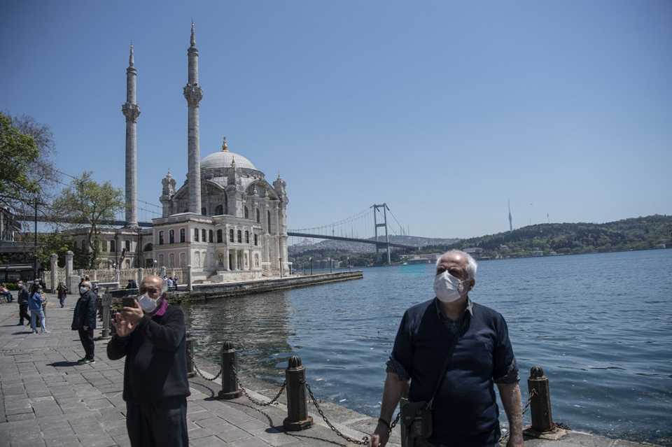 Elderly people wearing protective face masks, stroll along the seaside near the Buyuk Mecidiye mosque, also known as ortakoy mosque on May 10, 2020, at Ortakoy in Istanbul.