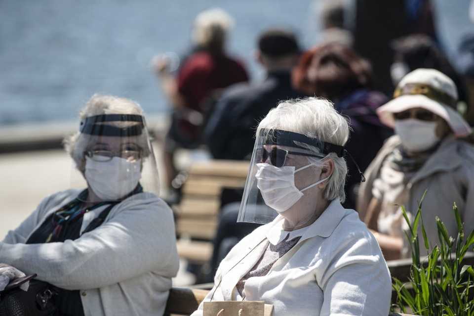 Women wearing protective face masks, sit at a required social distance along the seaside on May 10, 2020, at Kabatas in Istanbul.
