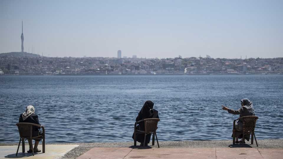 Women wearing protective face masks, sit apart following social distancing measures at the seaside on May 10, 2020, at Kabatas in Istanbul.