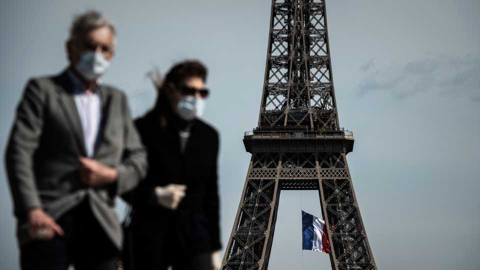 A man and a woman wearing face masks walk on Trocadero Plaza as a French national flag flies on the Eiffel Tower in the background in Paris on May 11, 2020.