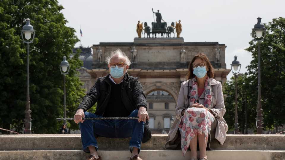 People wear a protective masks rest next the closed Tuileries garden in Paris, Tuesday, May 12, 2020.