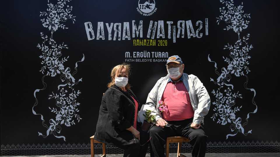 An elderly couple wearing protective face masks, pose for a photograph on a stage during a event in a park in the Fatih district of Istanbul on May 24, 2020, after a month and a half of lockdown restrictions aimed at stemming the spread of Covid-19.