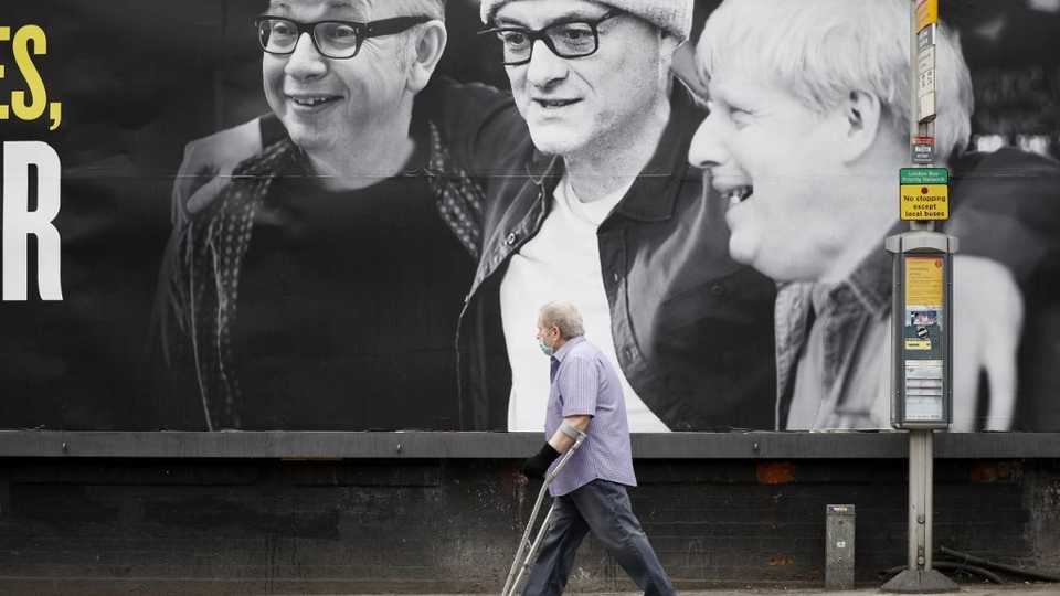 A man wearing a facemask walks past a billboard featuring (L-R) Britain's Chancellor of the Duchy of Lancaster Michael Gove, Number 10 special advisor Dominic Cummings and Britain's Prime Minister Boris Johnson and posted by political campaign group 'Led By Donkeys' in Kentish Town, north west London on June 3, 2020.