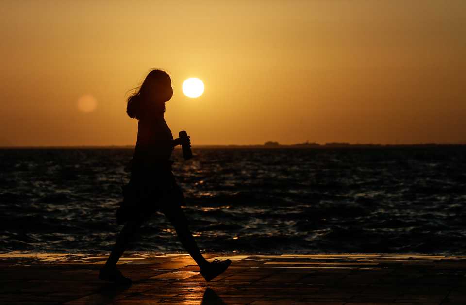 Silhouette of a girl wearing a face mask for protection against Covid-19 is seen near a coastline during sunset in Izmir, Turkey on June 07, 2020.