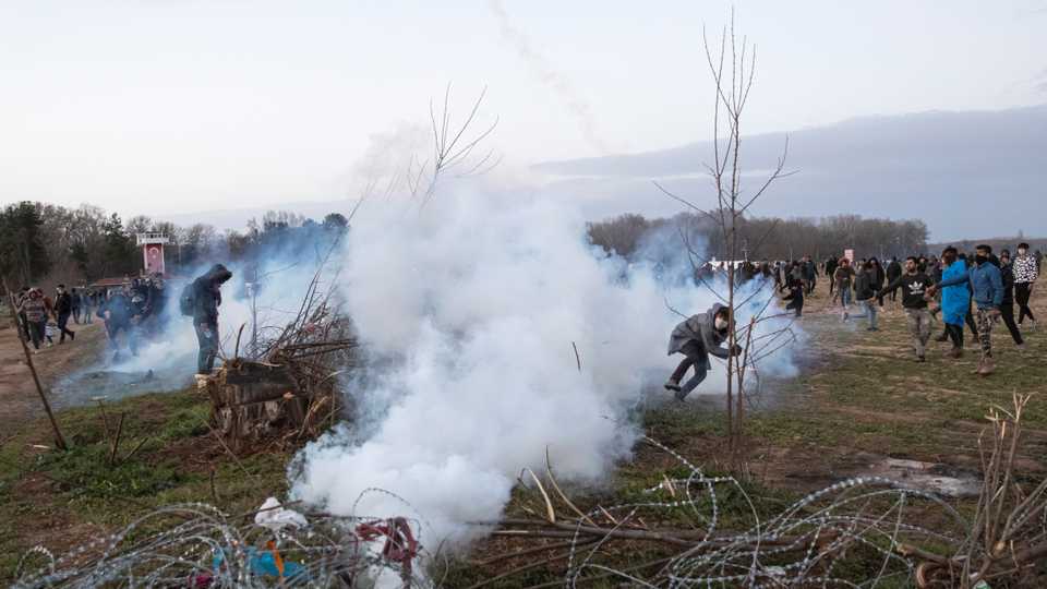 A migrant throws back a tear gas canister as they clash with Greek riot police on the Turkish-Greek border in Edirne, Turkey, March 7, 2020.