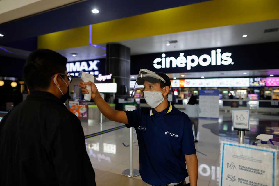 Cinema worker Gustavo Angel Oropeza Alvarez, 21, takes the temperature of a man arriving at the Cinepolis movie theaters in Forum Buenavista mall, in Mexico City, Wednesday, August 12, 2020.
