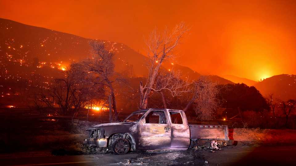 A scorched vehicle rests on Pine Canyon Rd. as the Lake Fire burns a hillside in the Angeles National Forest, California, north of Santa Clarita on Thursday, August 13, 2020.