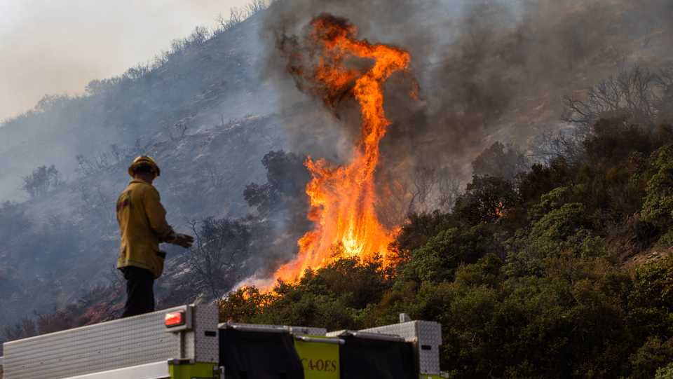 A Riverside firefighter stands on top of his truck during the Lake Fire at Pine Canyon Road in the Angeles National Forest, by Lake Hughes, 60 miles north of Los Angeles, California on August 15, 2020.