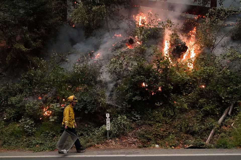 Ben Slaughter, a firefighter for the Boulder Creek Fire Department, walks along Highway 9 while monitoring flames from the CZU August Lightning Complex Fire, Saturday, August 22, 2020,.