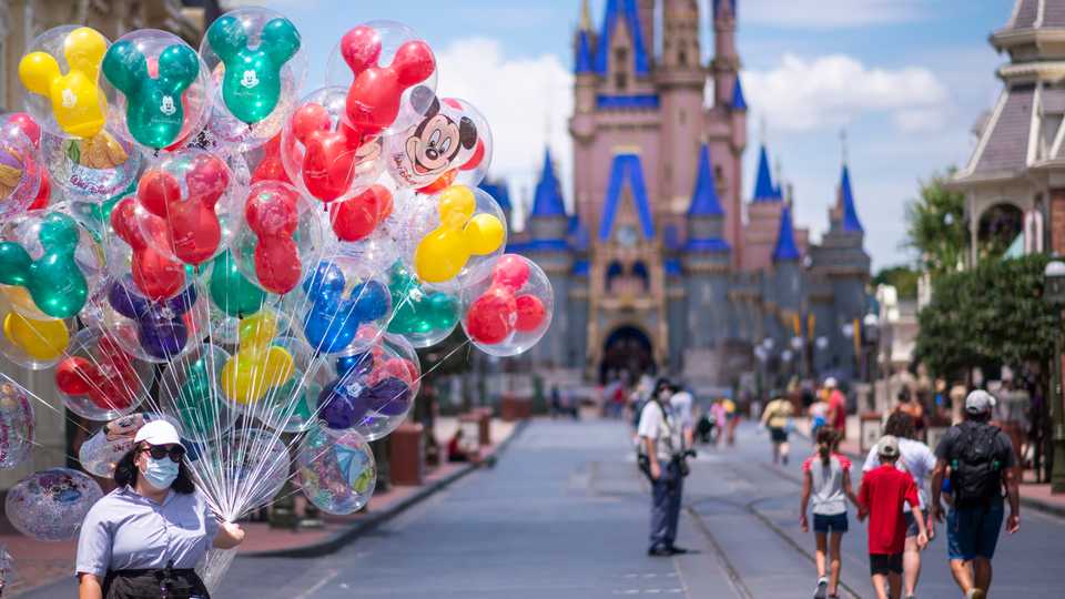 A balloon vendor wears a required face mask due to the Covid-19 pandemic on Main Street, USA in front of Cinderella Castle at Walt Disney World Resort's Magic Kingdom, August 12, 2020.