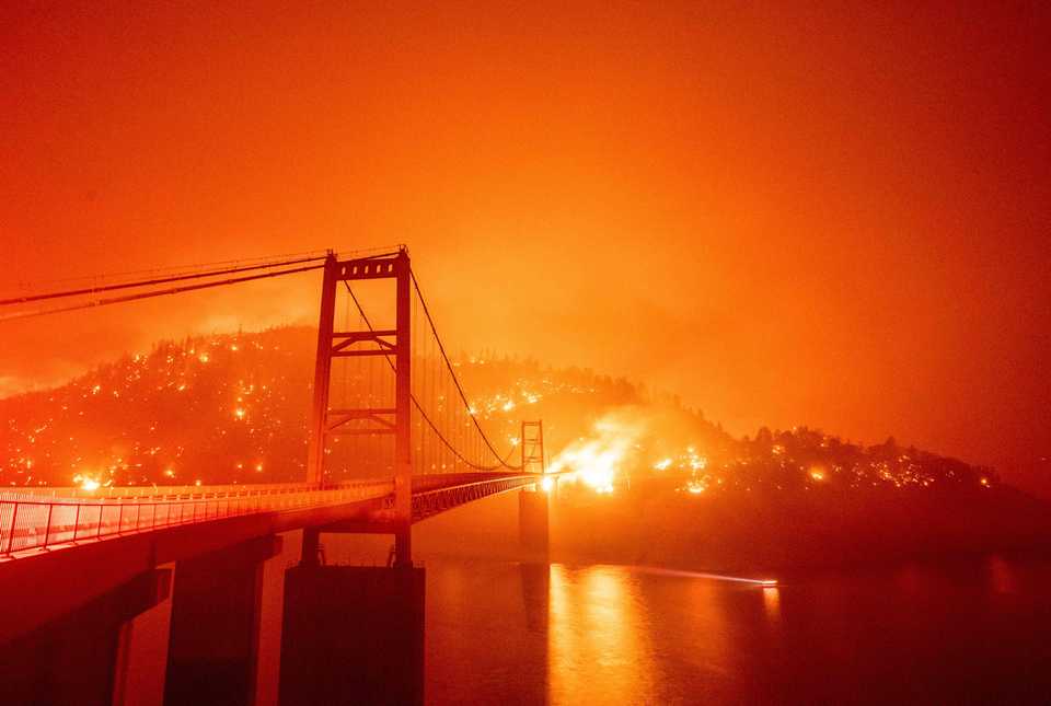 A boat motors by as the Bidwell Bar Bridge is surrounded by fire in Lake Oroville in California.