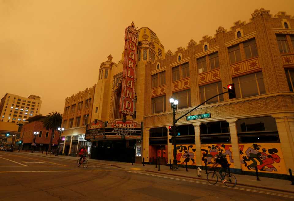 Bicyclists pass the Fox Theater on Telegraph Avenue as orange skies glow in downtown Oakland, Calif., on Wednesday, Sept. 9, 2020.