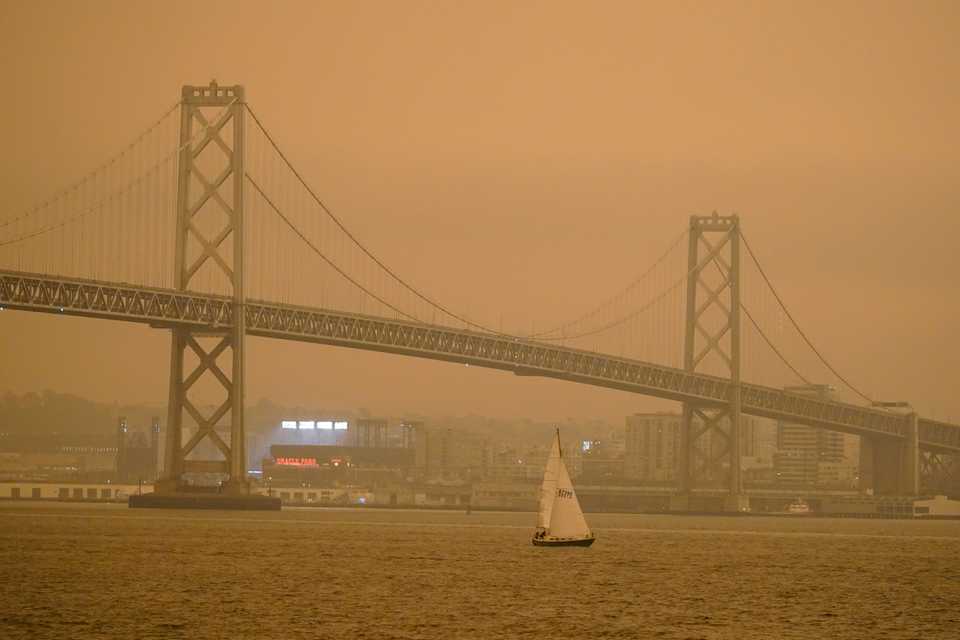 A sailboat makes its way past the San Francisco-Oakland Bay Bridge and lights at Oracle Park Wednesday, Sept. 9, 2020, in San Francisco.