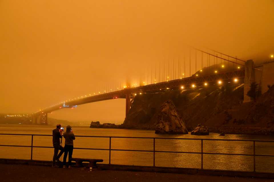 Patrick Kenefick, left, and Dana Williams, both of Mill Valley, Calif., record the darkened Golden Gate Bridge covered with smoke from wildfires Wednesday, Sept. 9, 2020, from a pier at Fort Baker near Sausalito, Calif. The photo was taken at 9:47 am in the morning.