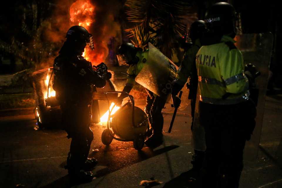 Police officers attempt to extinguish fire from a burning dumpster during a protests in Bogota, Colombia, September 10, 2020.