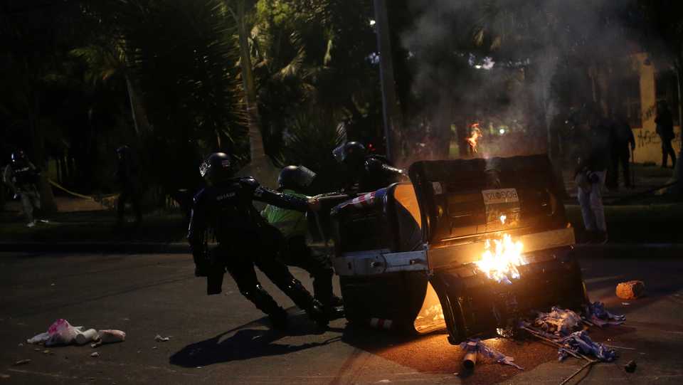 Police officers drag a burning dumpster away during a protest in Bogota, Colombia, September 10, 2020.