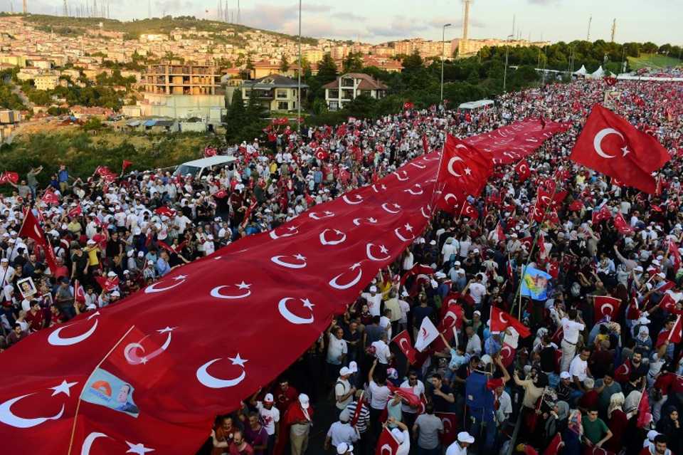 People stand under Turkey's national flag as they gather on the July 15 Martyrs Bridge in Istanbul on July 15, 2017. 