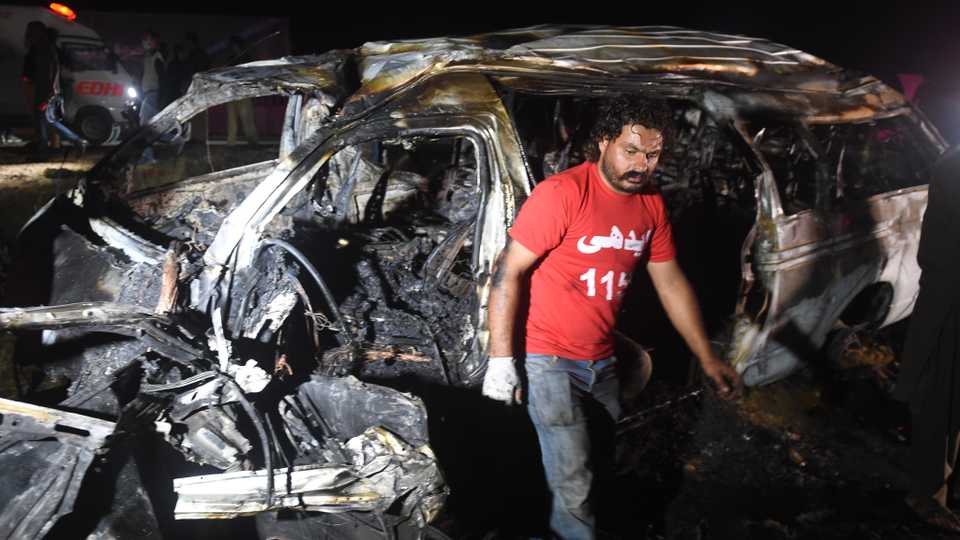 A volunteer walks past a burnt passenger van following an accident in the Nooriabad area on a highway some 50 km from Pakistan's port city of Karachi late on September 26, 2020.