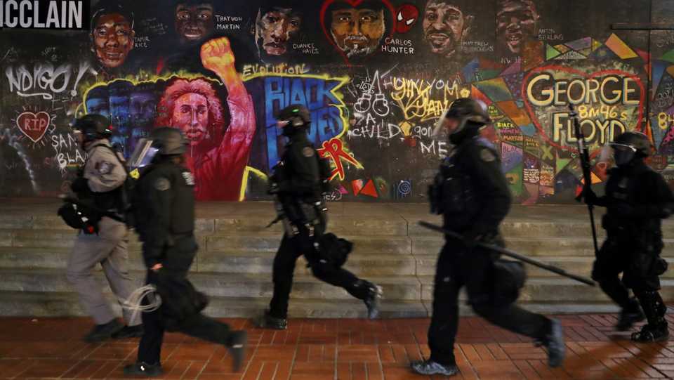 Police officers walk past graffiti during a protest against police violence and racial inequality in Portland, Oregon, US, September 27, 2020.