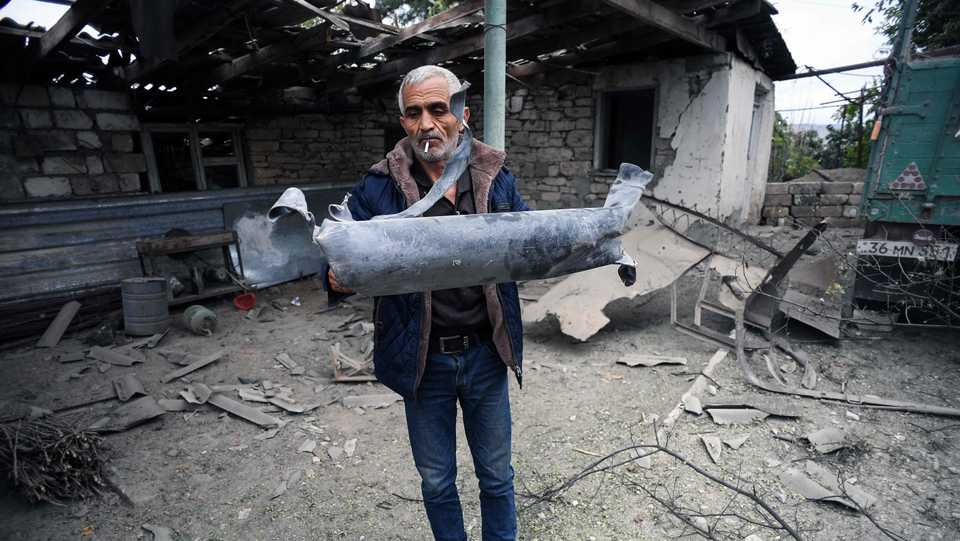 A man shows a shell fragment in the yard of his brother's house damaged by shelling during fighting between Armenia and Azerbaijan over occupied Karabakh in its Martuni city on October 1, 2020.
