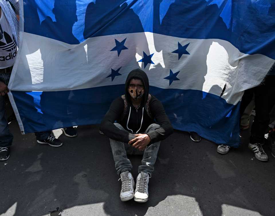 A Honduran migrant sits in front of a Honduran flag in Entre Rios, Guatemala, after crossing the border from Honduras on his way to the US in a caravan, October 1, 2020.
