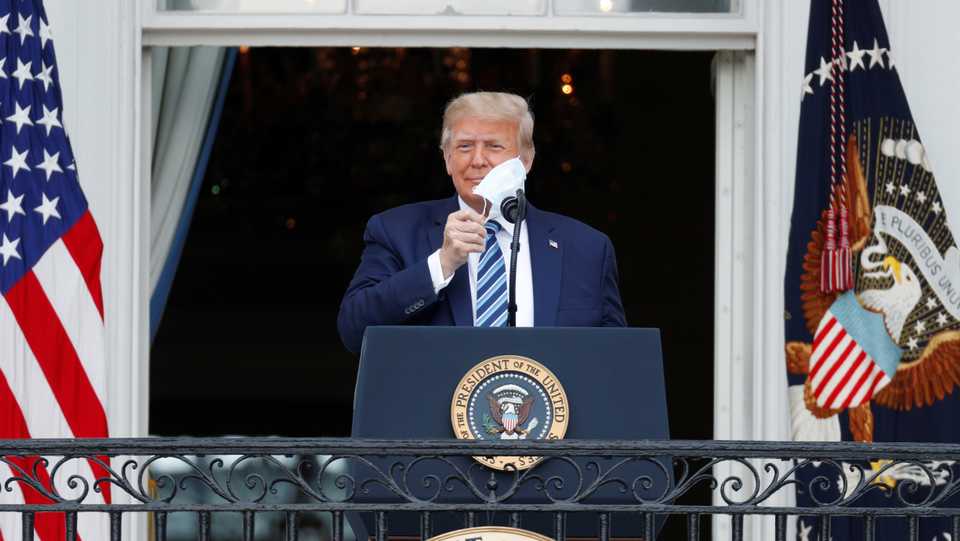 US President Trump takes off his face mask as he comes out on a White House balcony to speak to supporters in Washington on October 10, 2020.