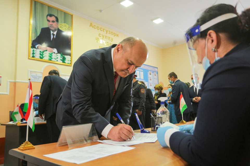 Presidential candidate of Agrarian Party Rustam Latifzoda receives a ballot at a polling station during the presidential election, with a portrait of Tajik President Emomali Rahmon in the background, in Dushanbe, Tajikistan, October 11, 2020.