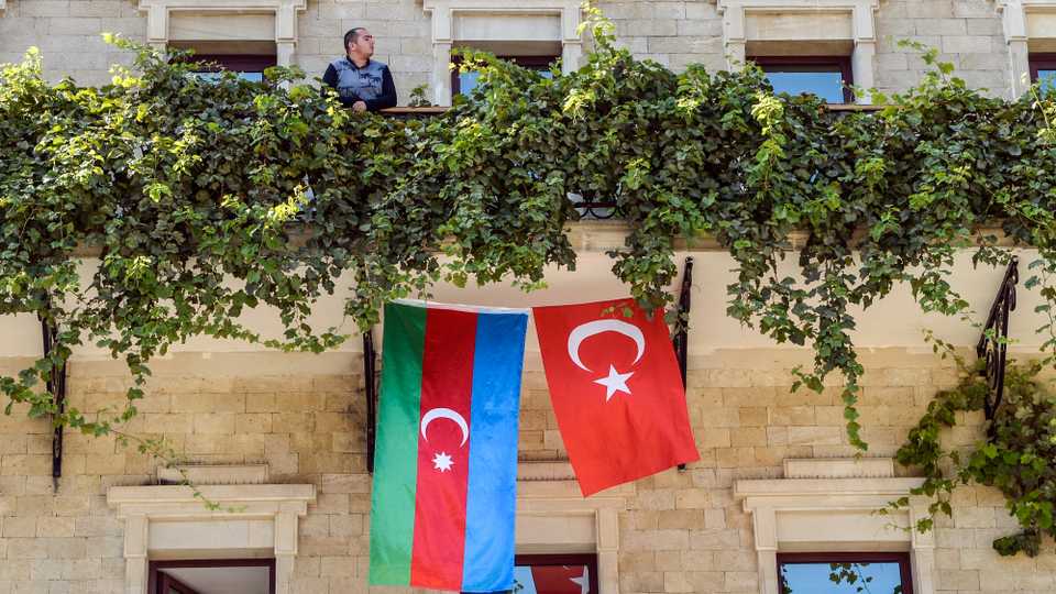 A man stands on the balcony of a hotel with its facade decorated with flags of Azerbaijan and Turkey in the Old Town of Baku on October 14, 2020.