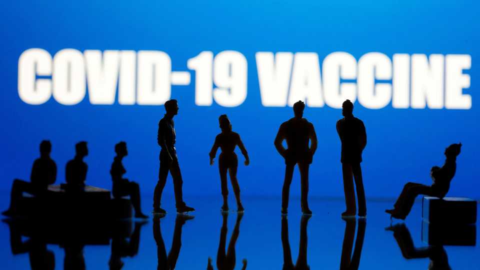 Small toy figures are seen in front of a Covid-19 Vaccine logo in this illustration taken on September 9, 2020.