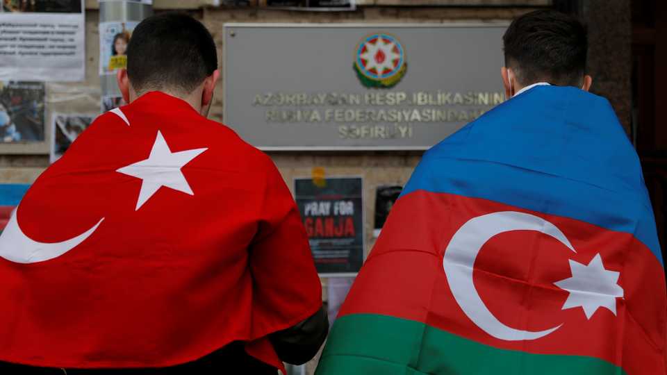 Men wearing the national flags of Azerbaijan and Turkey stand next to a makeshift memorial for people killed in Azerbaijan during the military conflict over the breakaway region of Nagorno-Karabakh, outside the Embassy of Azerbaijan in Moscow, Russia, on October 19, 2020.