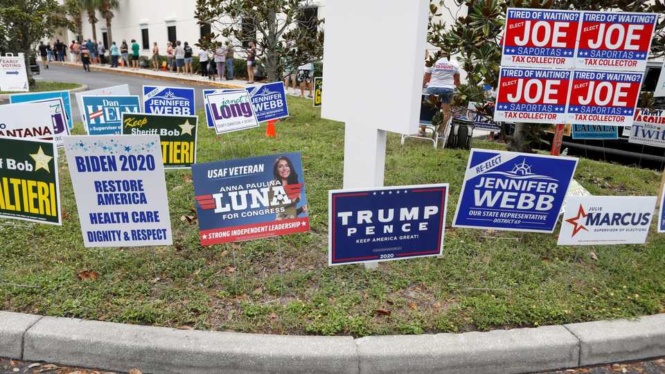 Campaign signs are posted near the Supervisor of Elections Office polling station while people line up for early voting in Pinellas County, ahead of the election in Largo, Florida, US, October 21, 2020.
