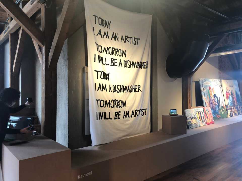Kavachi has worked as a dishwasher to survive as an artist overseas. In this display, the hand-stitched lettering says ‘Today I am an artist. Tomorrow I will be a dishwasher.’