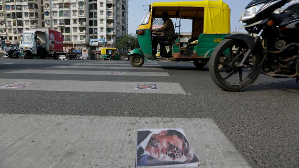 Indian commuters move on defaced images of French President Emmanuel Macron pasted by protestors on a road in Ahmedabad, India. November 1, 2020.