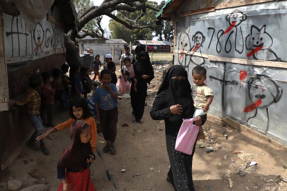 Rohingya refugee women walking past graffiti with their UN documents to a nearby verification center in Bathindi area of Jammu.