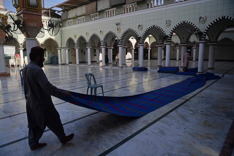 A volunteer places prayer mats on floor at a mosque ahead of Ramadan in Karachi on April 12, 2021.