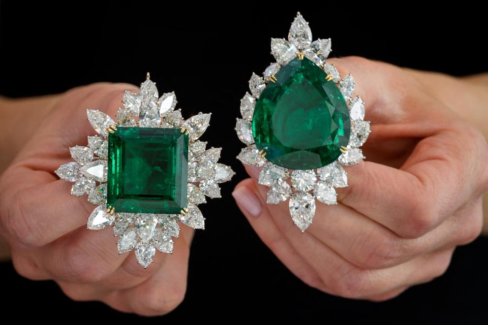 An model pose on May 6, 2021 with Right: an emerald and diamond brooch/pendant combination, Harry Winston, circa 1970, set with a pear-shaped emerald weighing 104.40 carats and Left: an emerald and diamond brooch/pendant combination Harry Winston, set with a step-cut emerald weighing 80.45 carats during a press preview ahead of sales by Sotheby's auction house on May 11, 2021 in Geneva.