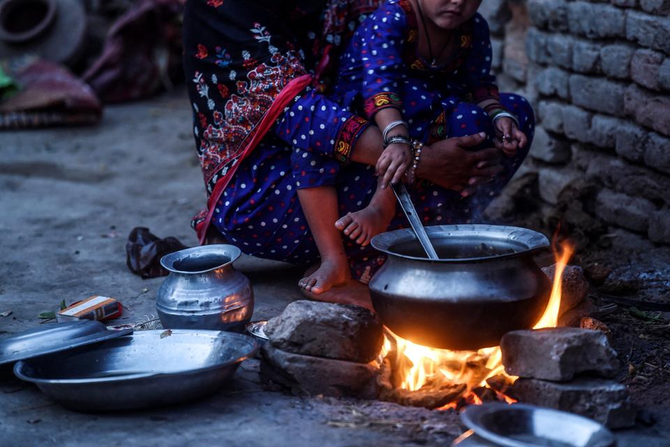 In this picture taken on March 25, 2021, Hakima Shar, who is HIV positive, cooks food for her family with her HIV positive daughter on her lap at their home in Subhani Shar village near Rato Dero, in southern Sindh province.