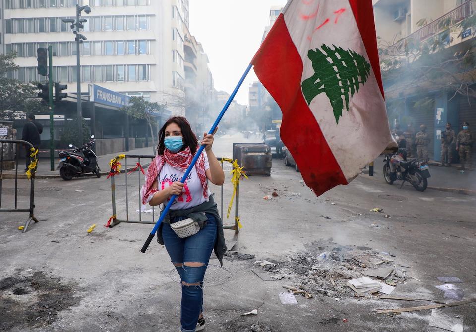 A demonstrator carries a national flag along a blocked road, during a protest against the fall in Lebanese pound currency and mounting economic hardships, near the Central Bank building, in Beirut, Lebanon March 16, 2021.