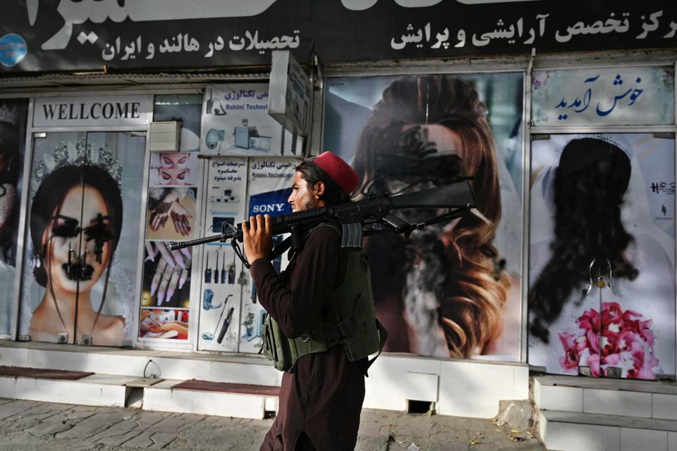 A Taliban fighter walks past a beauty salon with images of women defaced using spray paint in Shar-e-Naw in Kabul on August 18, 2021.
