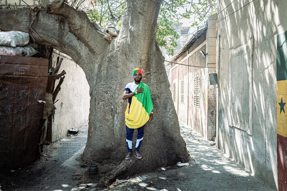 In one of Dakar’s oldest neighbourhoods, 24-year old soccer fan Bamba Dieng stands in front of a baobab tree said to have cleared the quarters from bad spirits. To Bamba, football is intrinsically linked to immigration. ‘’Football has helped Senegalese make it big internationally by migrating, ’’he says.