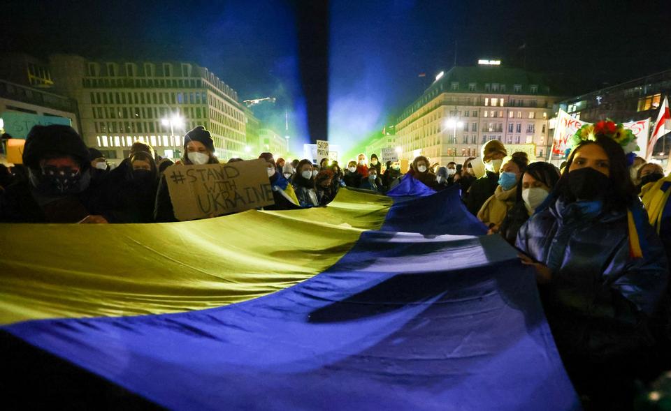 People carry banners and a Ukrainian flag at a square beside the Brandenburg Gate during a protest, after Russia launched a massive military operation against Ukraine.