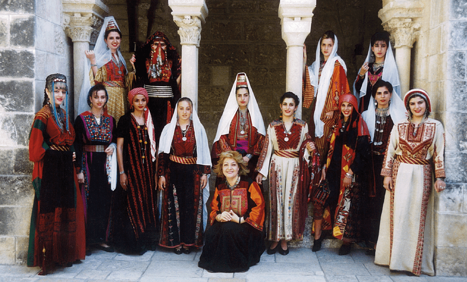 Palestinian women wearing traditional dresses representing Palestinian villages and cities.