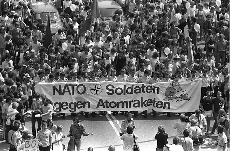 West German soldiers and civilians march with a banner reading