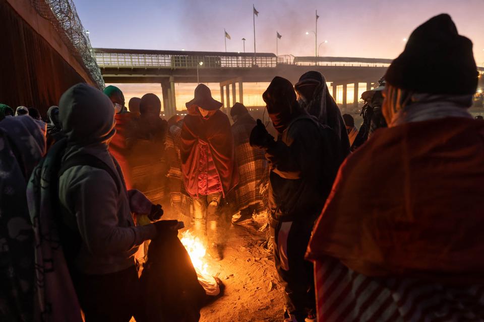 Immigrants warm by a fire at dawn after spending a night alongside the US-Mexico border fence  in El Paso, Texas.