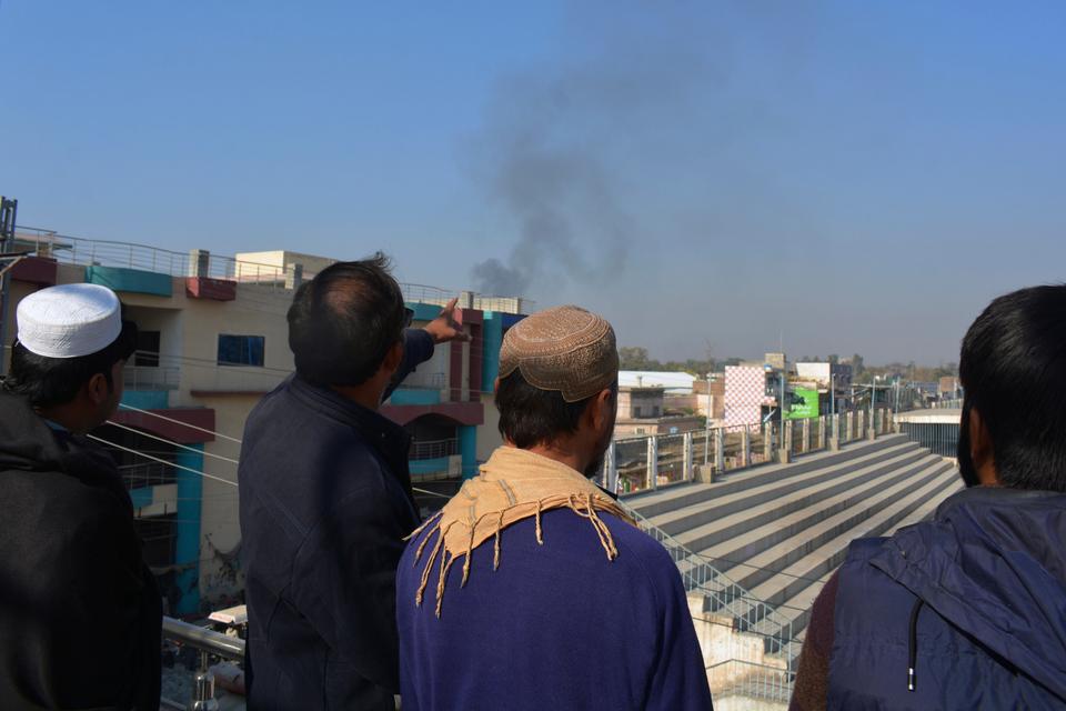 Local residents watch smoke rising from a counter-terrorism centre after security forces started to clear the compound seized by Pakistani Taliban in Bannu on December 20, 2022.
