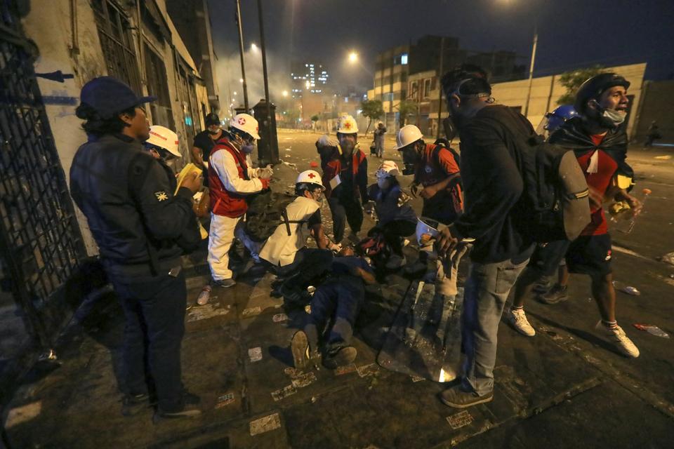 An injured demonstrator receives medical attention during clashes with riot police within a protest against the government.