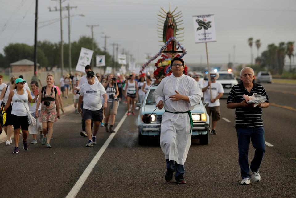 Alter server Anthoney Saenz, second from right, waves incense as he helps lead a procession toward the Rio Grande to oppose the wall the US government wants to build on the river separating Texas and Mexico, Saturday, Aug. 12, 2017, in Mission, Texas.