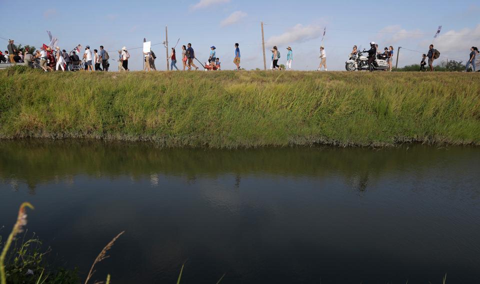 Hundreds of people march along a levee in South Texas toward the Rio Grande to oppose the wall the U.S. government wants to build on the river separating Texas and Mexico, Saturday, Aug. 12, 2017, in Mission, Texas.